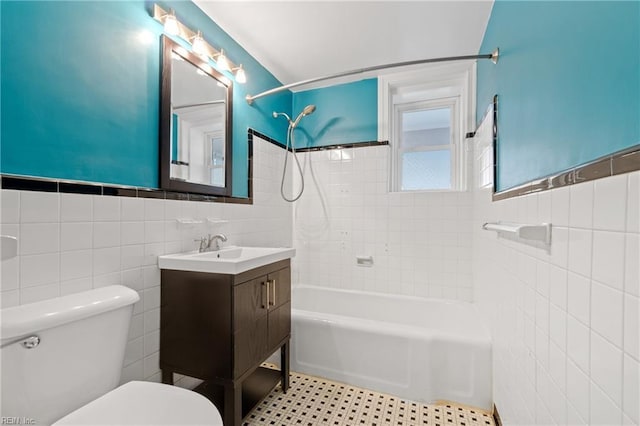 full bathroom featuring tiled shower / bath, vanity, toilet, and tile walls