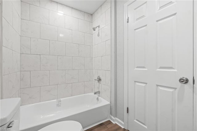 bathroom with hardwood / wood-style flooring, tiled shower / bath, and toilet