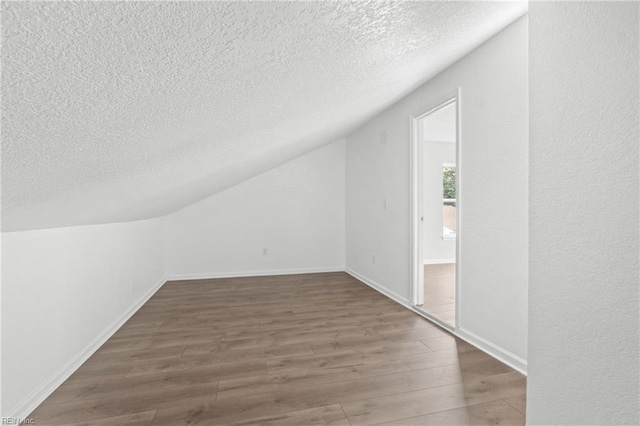 additional living space featuring lofted ceiling, dark hardwood / wood-style floors, and a textured ceiling