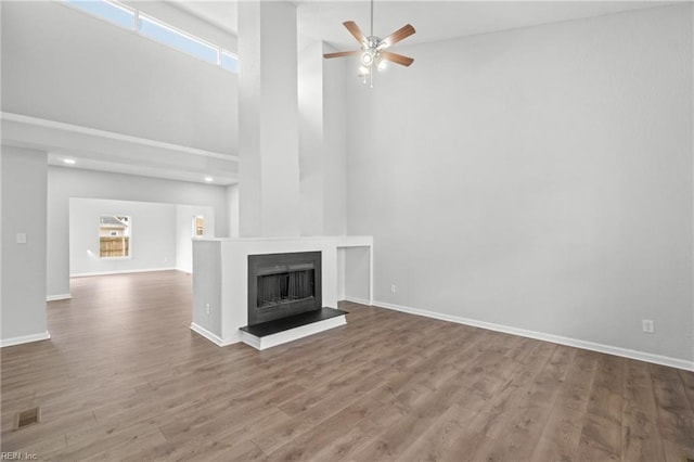 unfurnished living room featuring ceiling fan, wood-type flooring, and a high ceiling