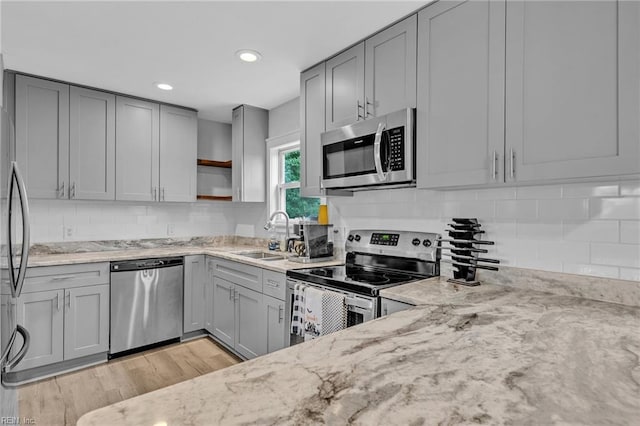 kitchen with stainless steel appliances, sink, light stone counters, and light hardwood / wood-style floors