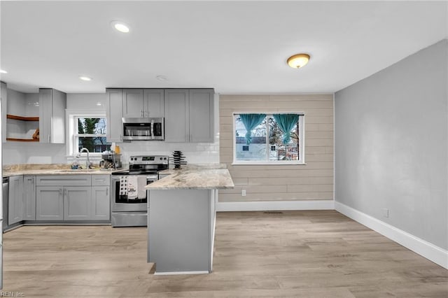 kitchen with appliances with stainless steel finishes, sink, kitchen peninsula, light stone countertops, and light hardwood / wood-style flooring