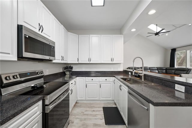 kitchen featuring sink, light hardwood / wood-style flooring, appliances with stainless steel finishes, vaulted ceiling with skylight, and white cabinets