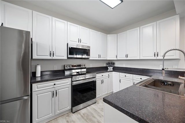 kitchen with stainless steel appliances, white cabinetry, sink, and light wood-type flooring