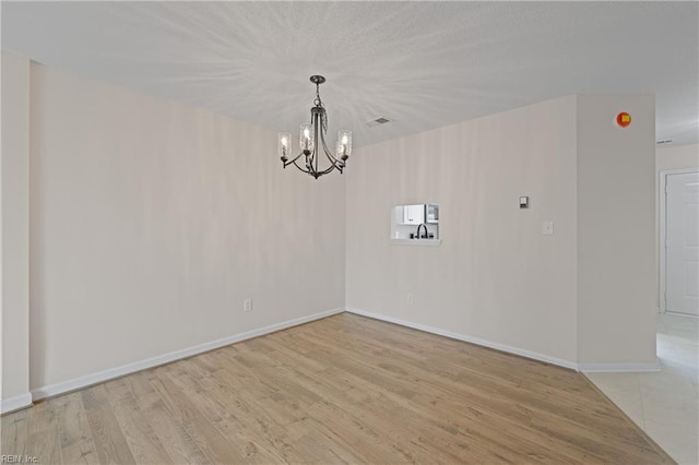 spare room with a notable chandelier and light hardwood / wood-style floors