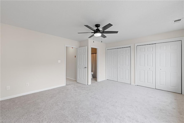 unfurnished bedroom featuring light carpet, two closets, and ceiling fan