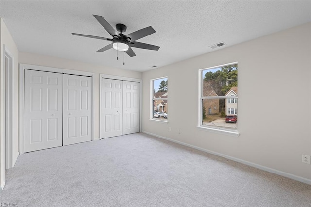 unfurnished bedroom with ceiling fan, two closets, light colored carpet, and a textured ceiling