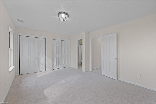 unfurnished bedroom featuring light carpet and multiple closets