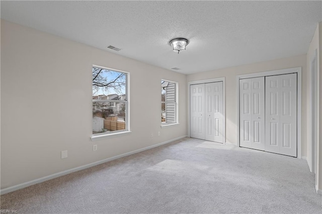 unfurnished bedroom featuring multiple closets, light colored carpet, and a textured ceiling