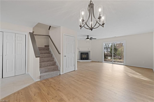 unfurnished living room with ceiling fan with notable chandelier and light hardwood / wood-style flooring