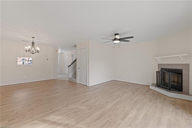 unfurnished living room featuring light wood-type flooring, ceiling fan with notable chandelier, and a fireplace