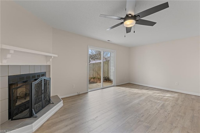 unfurnished living room with ceiling fan, a textured ceiling, a tile fireplace, and light hardwood / wood-style flooring