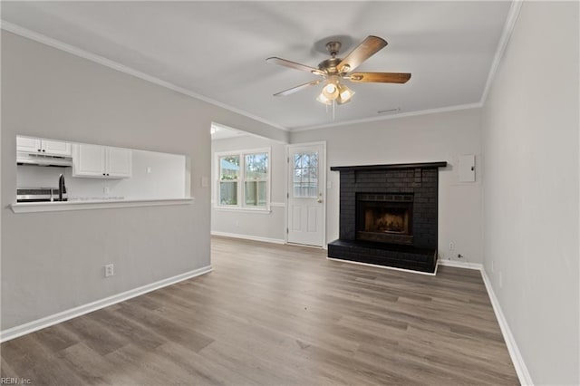 unfurnished living room featuring a brick fireplace, wood-type flooring, ornamental molding, and ceiling fan