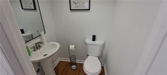 half bath featuring wood finished floors, toilet, and baseboards