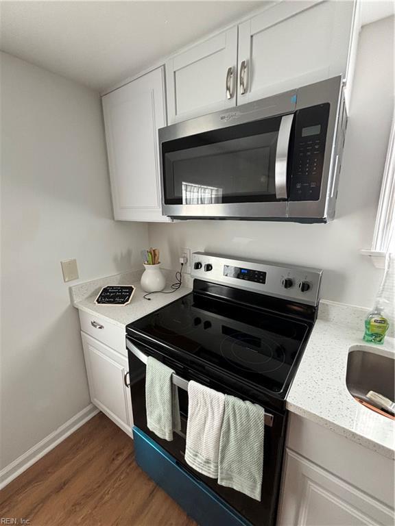 kitchen with appliances with stainless steel finishes, white cabinetry, sink, light stone counters, and dark wood-type flooring