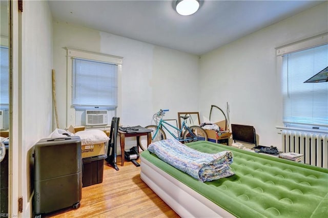 bedroom with cooling unit, radiator, and light hardwood / wood-style flooring