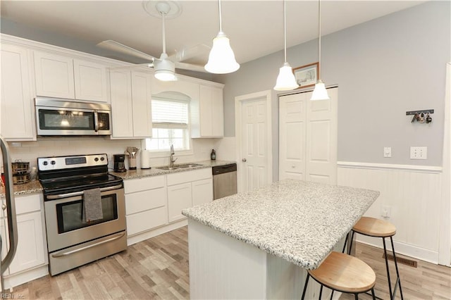 kitchen with sink, white cabinetry, appliances with stainless steel finishes, a kitchen island, and pendant lighting