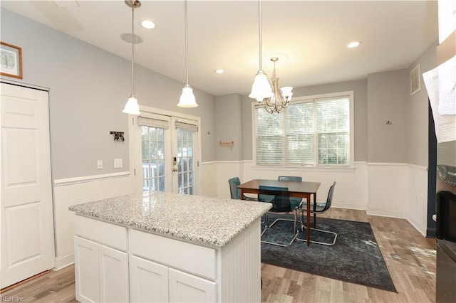 kitchen featuring decorative light fixtures, white cabinets, a center island, light stone counters, and light hardwood / wood-style flooring