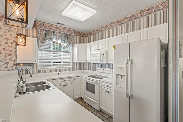 kitchen featuring sink, a textured ceiling, white appliances, and decorative light fixtures