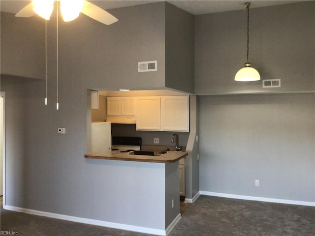 kitchen featuring dark colored carpet, decorative light fixtures, kitchen peninsula, white cabinets, and stove