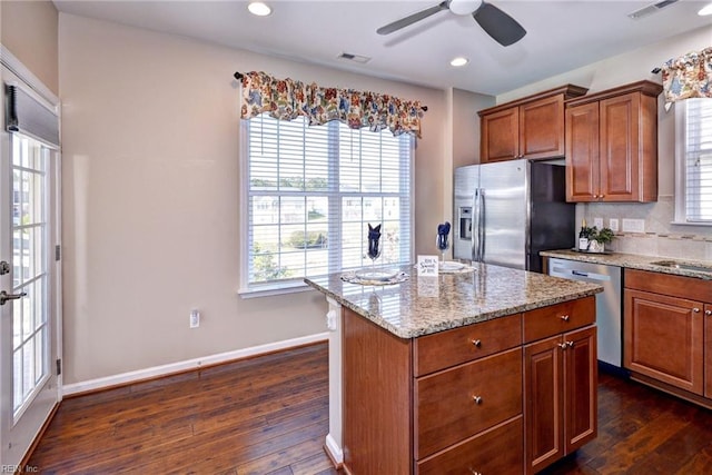 kitchen with appliances with stainless steel finishes, backsplash, dark hardwood / wood-style floors, a center island, and light stone counters