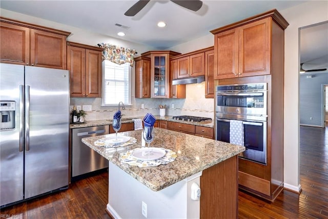 kitchen featuring dark wood-type flooring, a kitchen island, stainless steel appliances, light stone countertops, and decorative backsplash