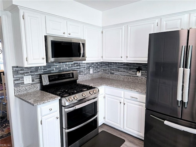 kitchen featuring white cabinetry, stainless steel appliances, wood-type flooring, and backsplash