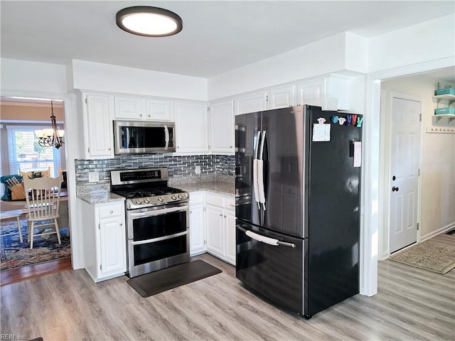 kitchen with appliances with stainless steel finishes, tasteful backsplash, white cabinets, light stone counters, and light hardwood / wood-style flooring