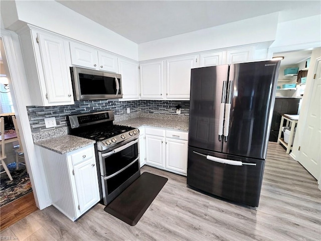 kitchen with white cabinetry, tasteful backsplash, appliances with stainless steel finishes, light stone countertops, and light hardwood / wood-style floors