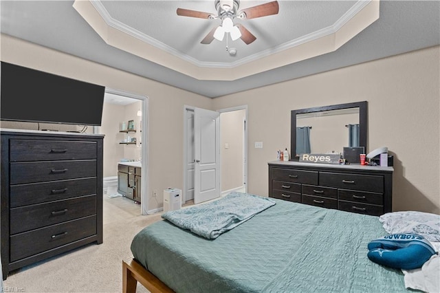 carpeted bedroom with ornamental molding, ensuite bathroom, ceiling fan, and a tray ceiling