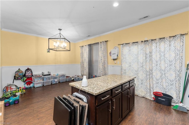 kitchen featuring dark wood-type flooring, hanging light fixtures, a center island, ornamental molding, and light stone countertops