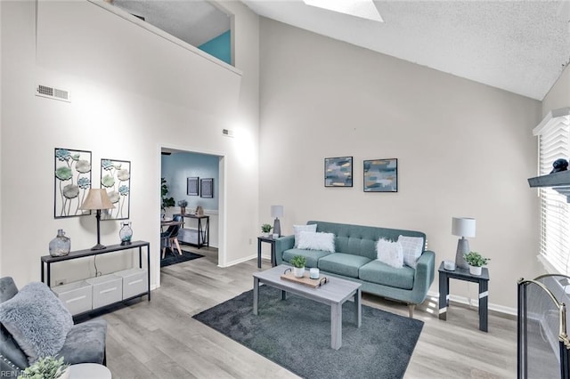 living room featuring a skylight, high vaulted ceiling, light hardwood / wood-style flooring, and a textured ceiling