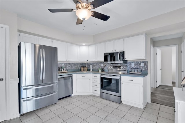 kitchen featuring appliances with stainless steel finishes, tasteful backsplash, white cabinets, light tile patterned floors, and ceiling fan