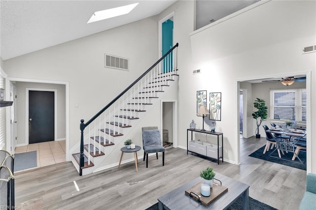 living room featuring ceiling fan, high vaulted ceiling, a skylight, and light hardwood / wood-style floors