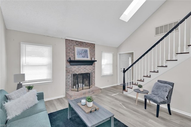 living room featuring vaulted ceiling with skylight, a fireplace, and hardwood / wood-style floors