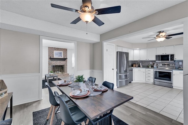 dining room featuring a brick fireplace, light hardwood / wood-style floors, a textured ceiling, and ceiling fan