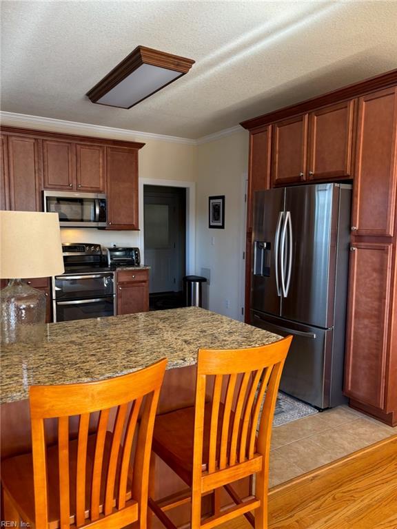 kitchen with a breakfast bar area, ornamental molding, light stone counters, kitchen peninsula, and stainless steel appliances