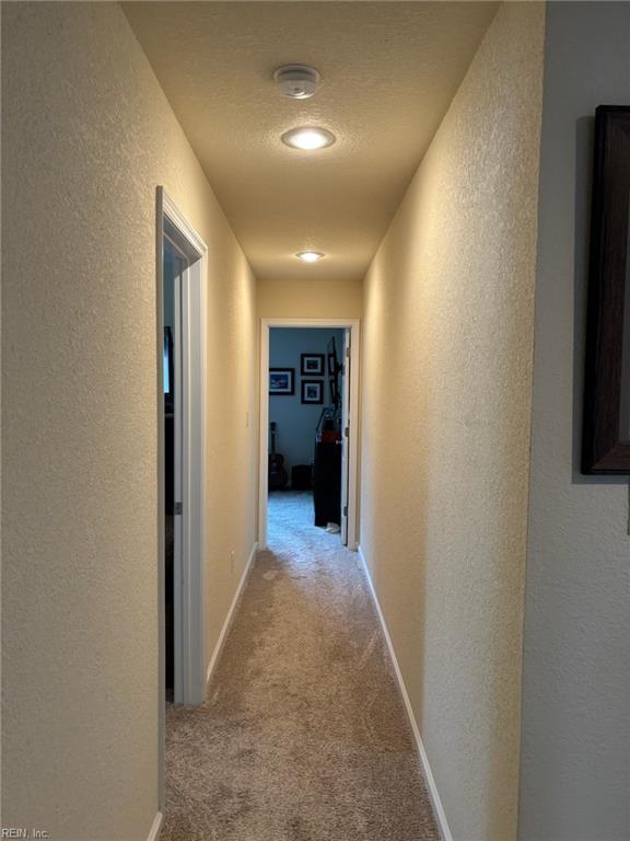 hallway with light colored carpet and a textured ceiling