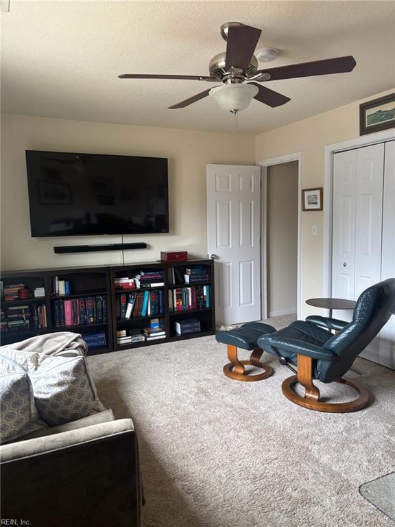 living room with ceiling fan, carpet floors, and a textured ceiling