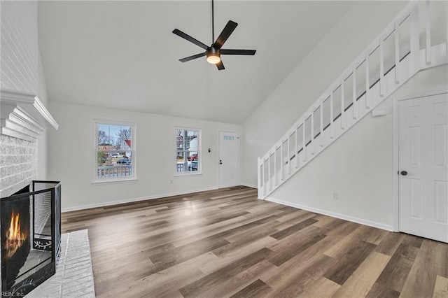 unfurnished living room featuring hardwood / wood-style flooring, vaulted ceiling, a brick fireplace, and ceiling fan