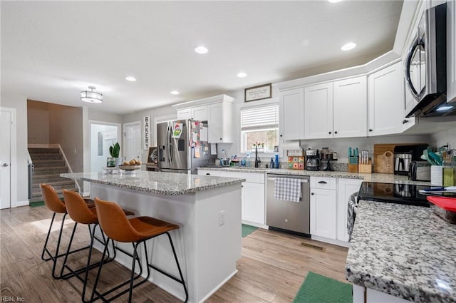 kitchen with appliances with stainless steel finishes, white cabinetry, a center island, light stone counters, and a kitchen bar