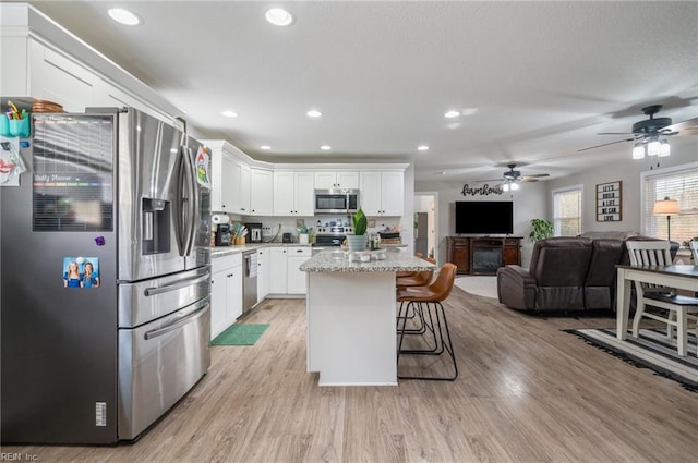 kitchen featuring white cabinetry, stainless steel appliances, a kitchen breakfast bar, light stone counters, and a kitchen island