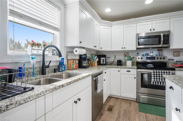 kitchen with sink, light wood-type flooring, appliances with stainless steel finishes, light stone countertops, and white cabinets