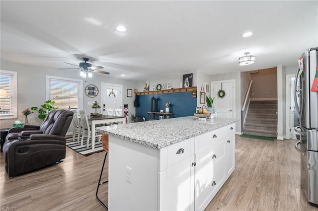 kitchen featuring white cabinetry, light stone counters, light hardwood / wood-style flooring, stainless steel fridge, and a kitchen island