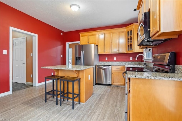 kitchen featuring appliances with stainless steel finishes, a kitchen bar, a center island, light stone countertops, and light wood-type flooring