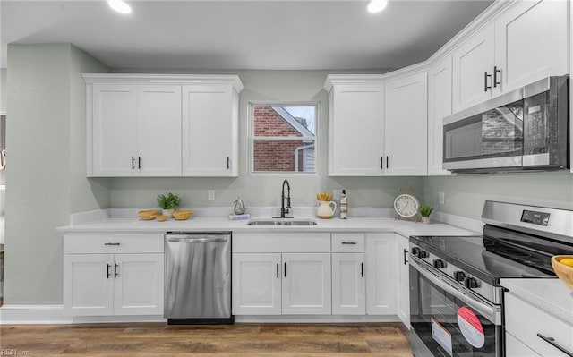 kitchen with white cabinetry, appliances with stainless steel finishes, a sink, and wood finished floors