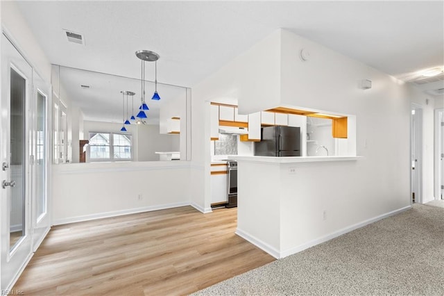 kitchen featuring stainless steel range with electric stovetop, decorative light fixtures, black refrigerator, kitchen peninsula, and white cabinets