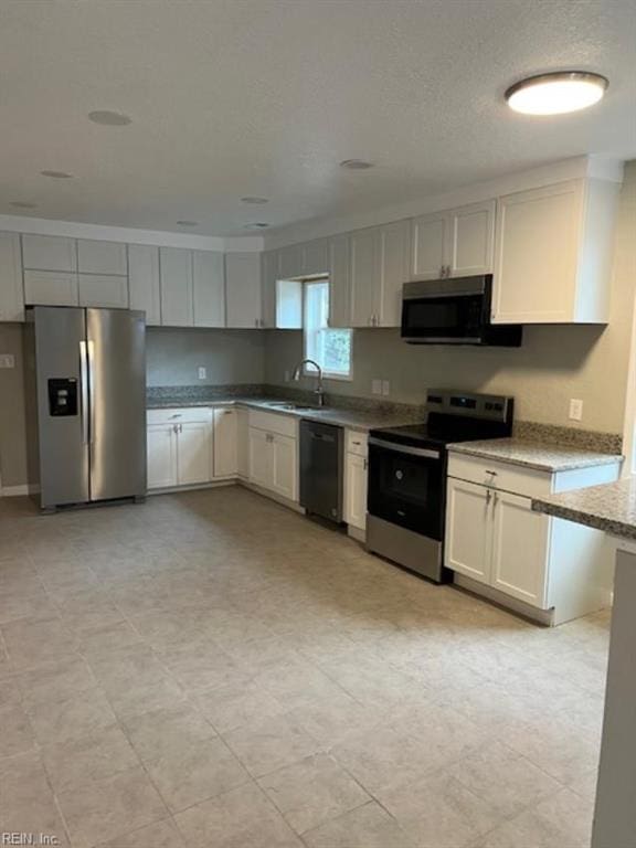 kitchen with sink, stainless steel appliances, light stone counters, a textured ceiling, and white cabinets