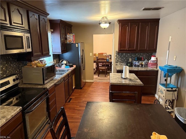 kitchen with appliances with stainless steel finishes, hardwood / wood-style floors, hanging light fixtures, a center island, and decorative backsplash