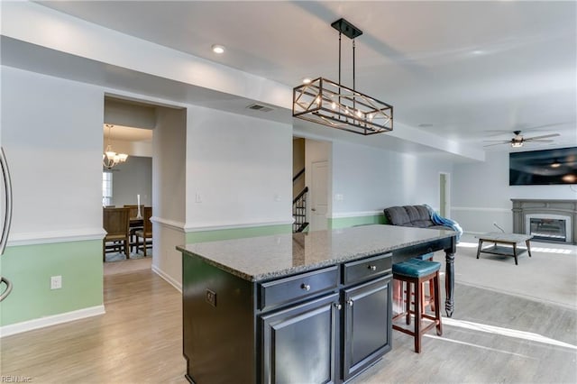 kitchen with a breakfast bar area, light hardwood / wood-style flooring, a center island, light stone counters, and decorative light fixtures